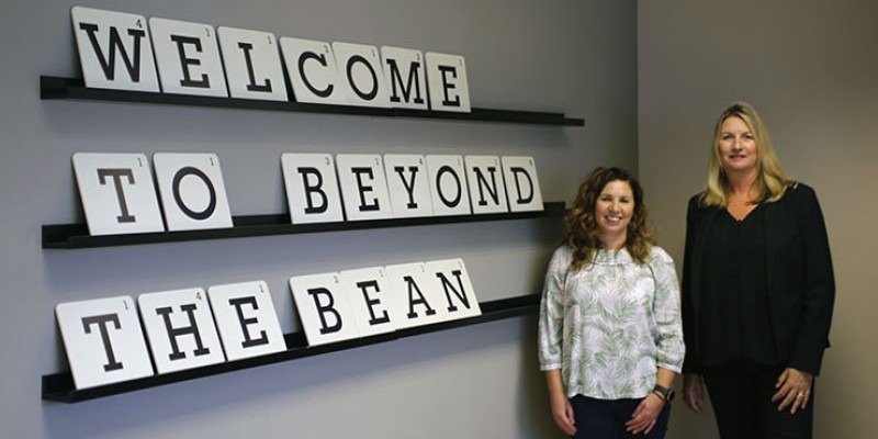 Katrina and Catherine Stephens standing beside a sign reading "Welcome to beyond the bean"